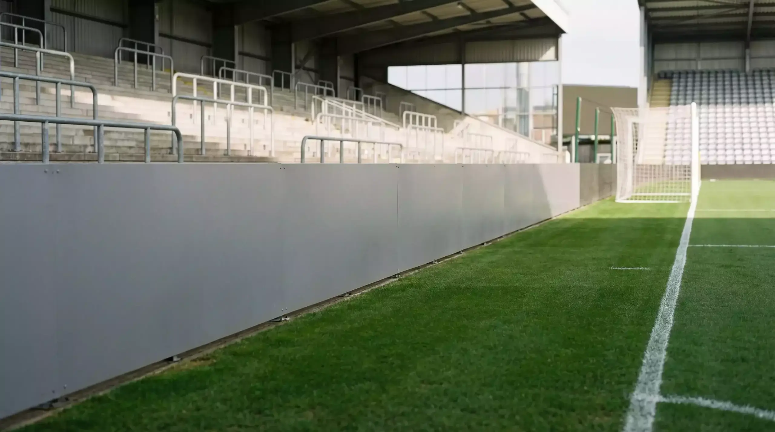 Valla publicitaria vacía junto a un campo de fútbol con gradas al fondo
